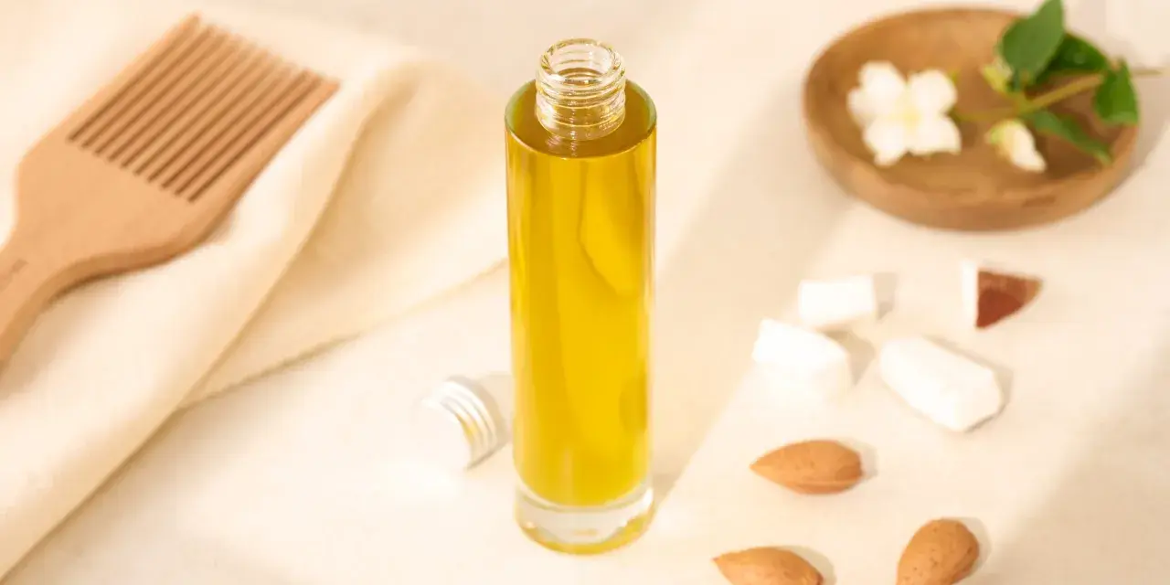 Bouteille d'huile d'amande douce pour les cheveux, avec un peigne en bois, des amandes et des fleurs de jasmin.