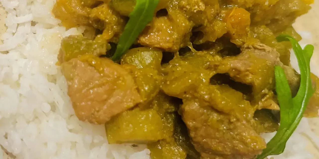 Un plat de riz blanc garni d'un curry vert aux légumes et morceaux de viande.