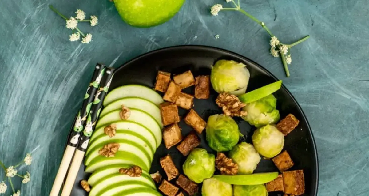 Salade colorée avec des tranches de pomme verte, des choux de Bruxelles, des dés de tofu croustillant et des noix, le tout arrosé d'une vinaigrette miso.