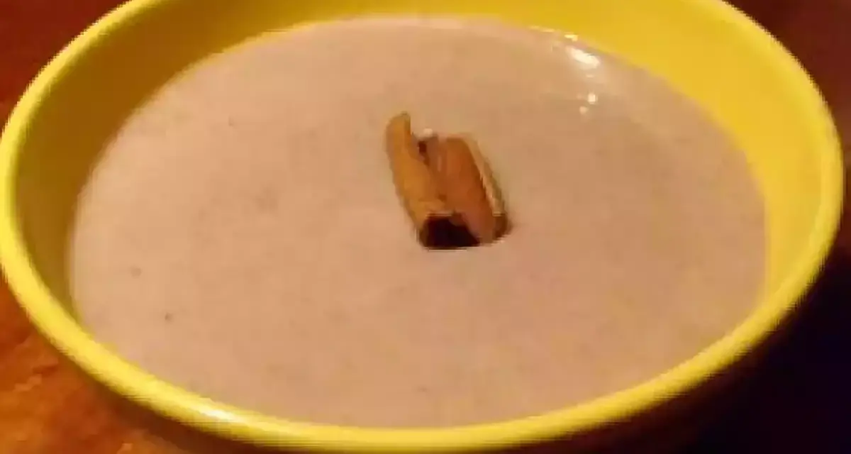 Un bol jaune contient une crème onctueuse de banane au lait de coco, garnie d'un bâton de cannelle.