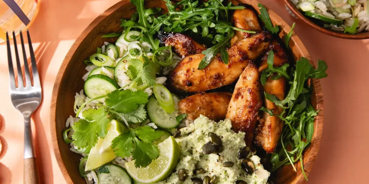 Un bol de riz au miso avec poulet glacé, concombre, coriandre, roquette et une purée verte parsemée de graines.