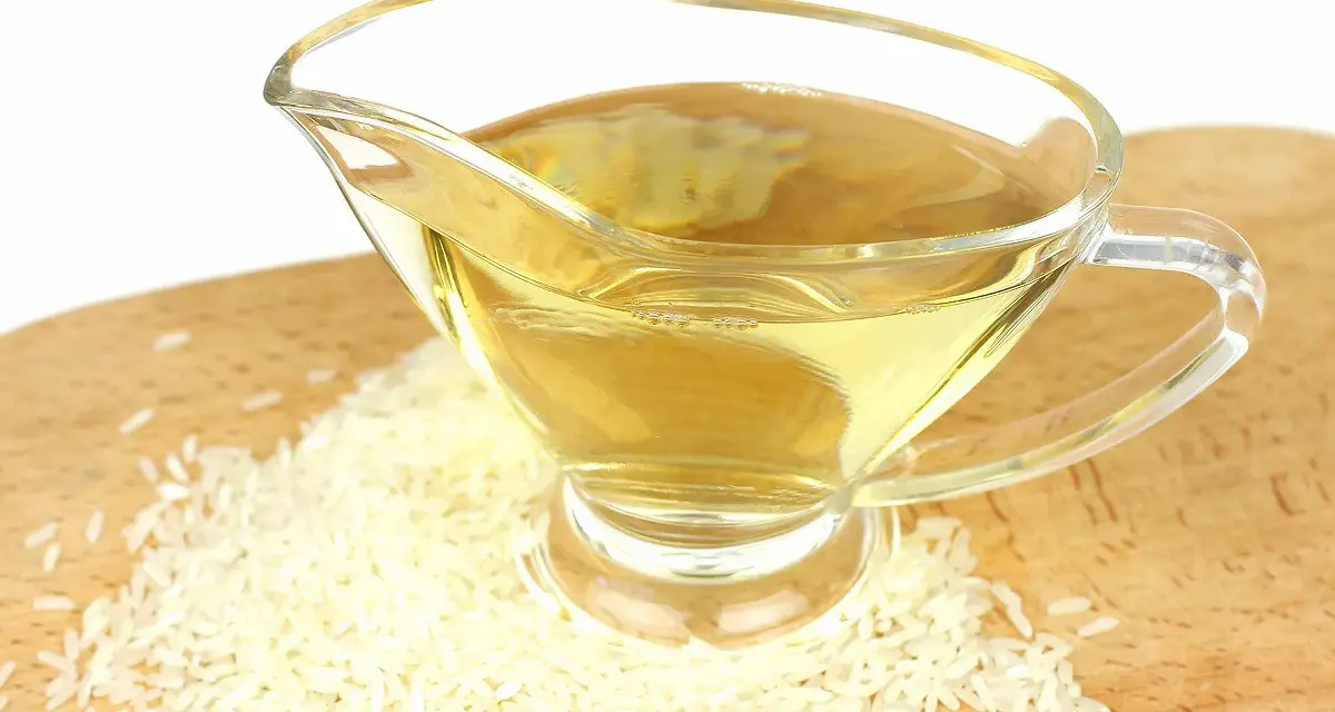 Un vinaigrier en verre rempli de liquide doré, entouré de grains de riz. Une idée pour par quoi remplacer le vinaigre de riz.