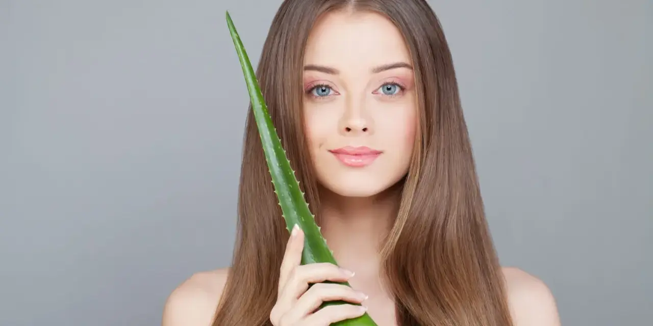 Une jeune femme aux cheveux longs tient une feuille d'aloe vera, montrant comment utiliser l'aloe vera pour une peau éclatante.