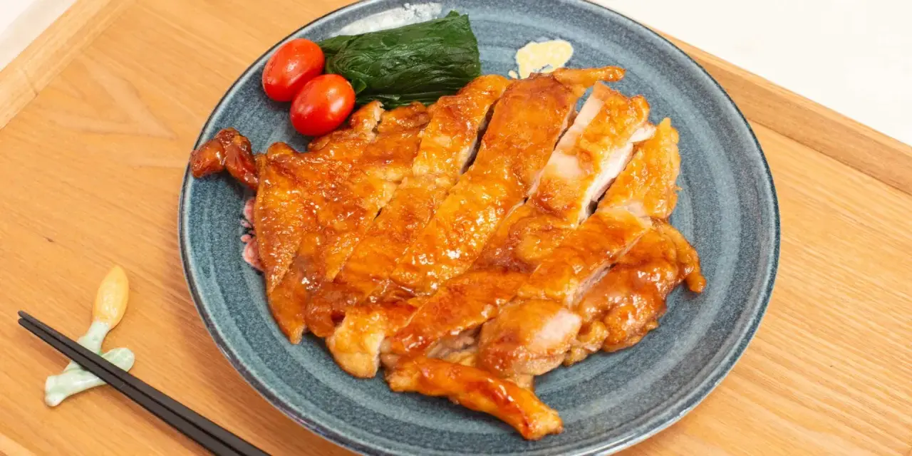 Délicieux poulet teriyaki recette, tranché et glacé, servi avec des tomates cerises et des épinards sur une assiette bleue.