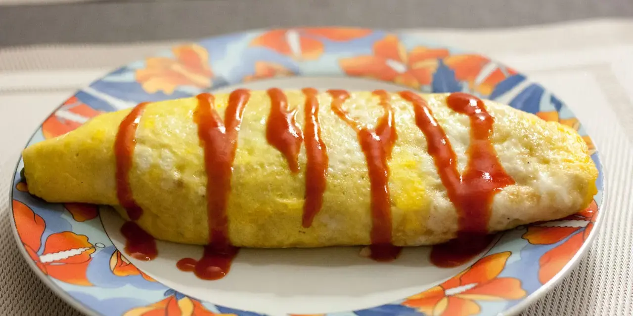 Une omelette japonaise au riz, nappée de ketchup, sur une assiette décorée de fleurs.