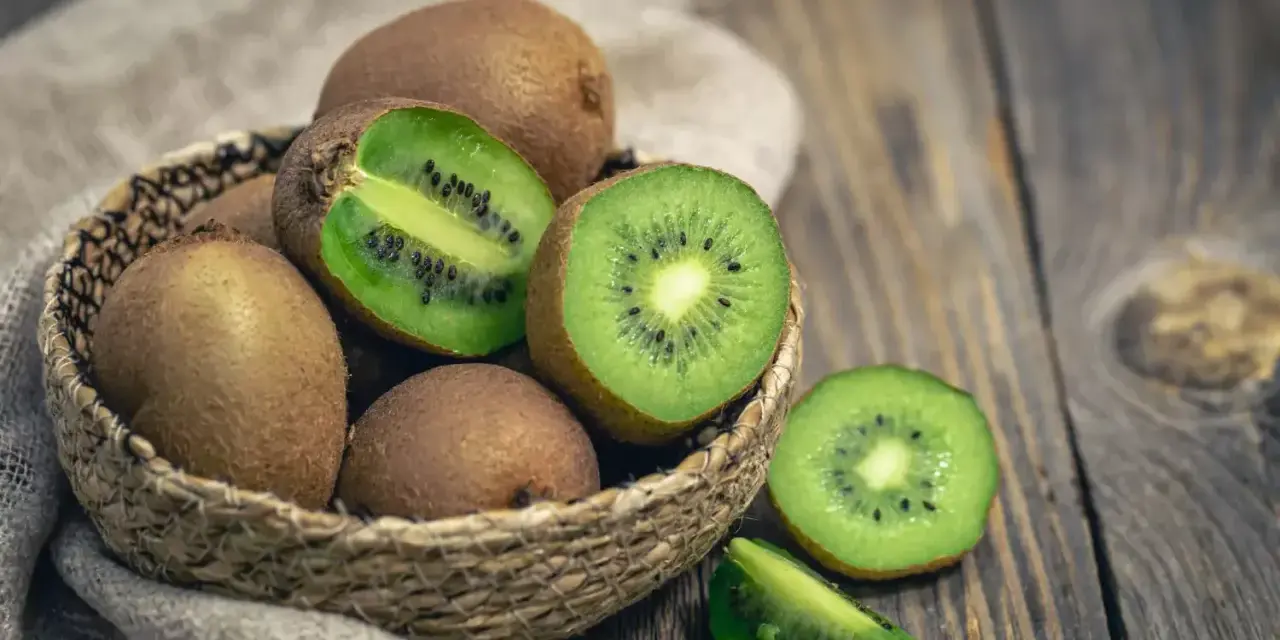 Un panier de kiwis frais, certains entiers, d'autres coupés, révélant leur chair verte et leurs pépins noirs. Attention, le kiwi peut provoquer une allergie.