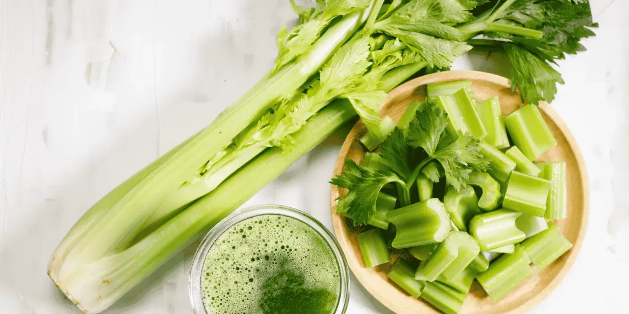 Jus de céleri frais, coupé en morceaux dans un bol en bois. Une branche entière de céleri est à côté. Attention à l'allergie céleri.