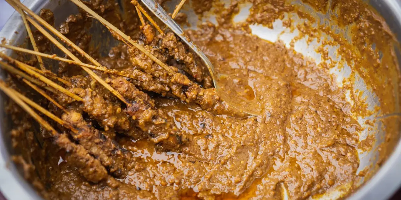 Brochettes de poulet baignant dans une généreuse sauce satay crémeuse, prêtes à être dégustées.