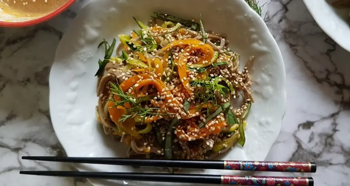 Salade de nouilles soba colorée avec des carottes, des courgettes et des graines de sésame, servie avec une sauce crémeuse.
