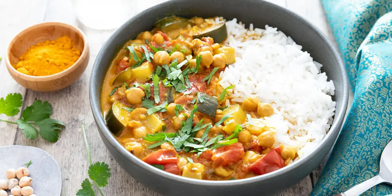 Un délicieux curry végétarien aux pois chiches, courgettes et tomates, servi avec du riz blanc et garni de coriandre fraîche.
