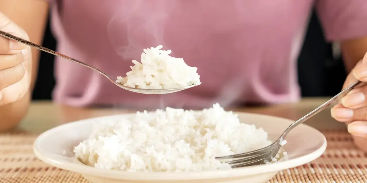 Une cuillère de riz blanc fumant, résultat d'une cuisson parfaite, est soulevée au-dessus d'une assiette remplie.