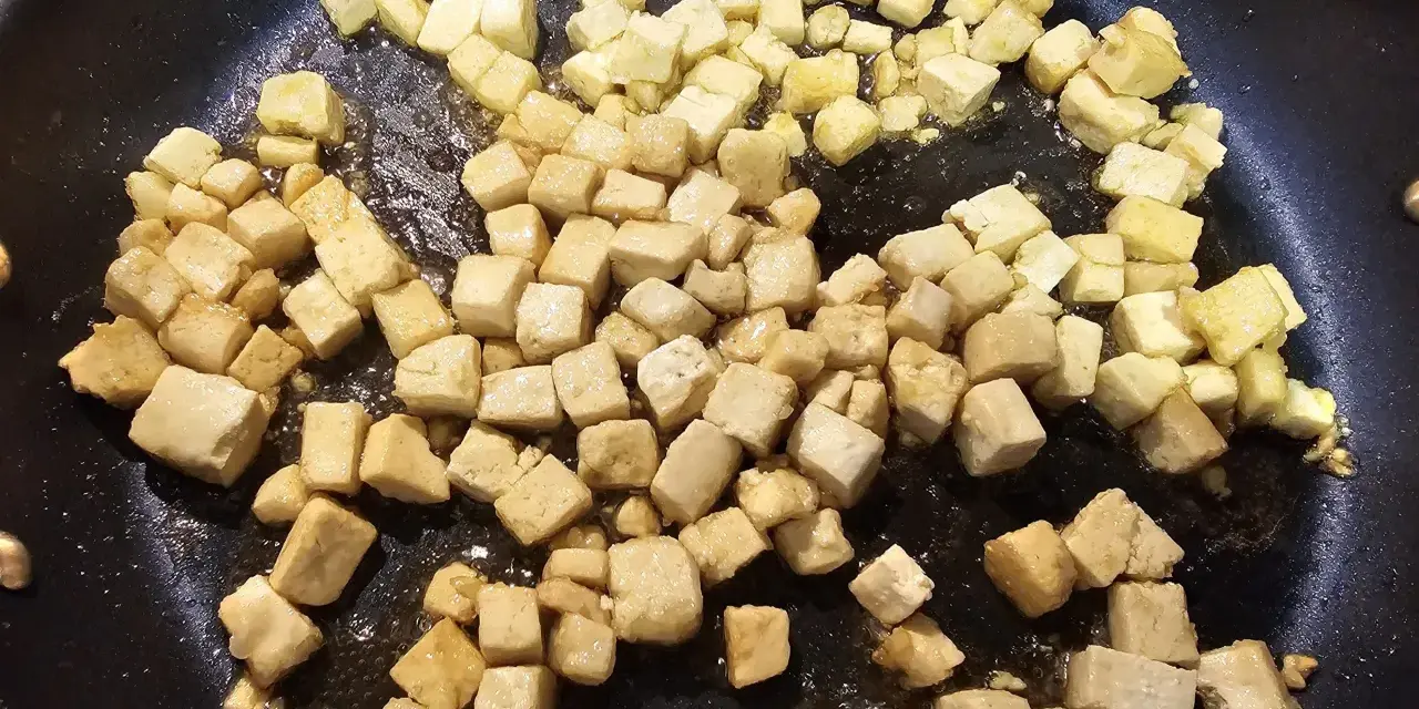 Dés cubes de tofu caramélisé dorent dans une poêle, prêts à être dégustés.