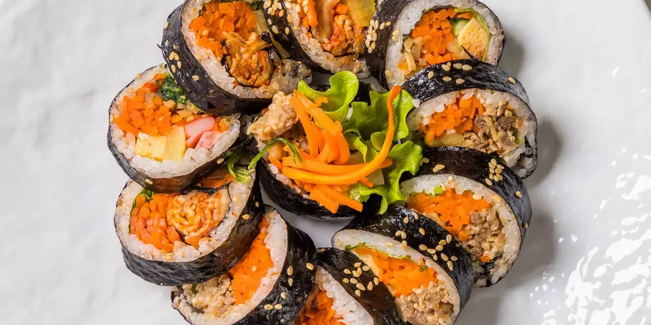 Un assortiment de makis végétariens colorés, garnis de carottes râpées, d'omelette et de légumes croquants, disposés en cercle sur une assiette blanche.