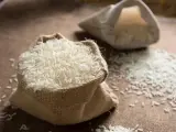 Un sac en toile de jute déborde de riz blanc, une céréale essentielle. Une autre bourse de riz est visible en arrière-plan.