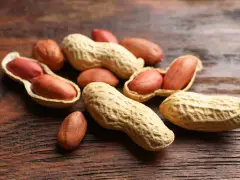 Un tas de noisettes arachides, certaines ouvertes révélant leurs grains rouges, sur un fond de bois sombre.