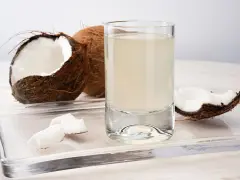 Un verre d'eau de coco, entouré de morceaux de noix de coco fraîches. Découvrez les nombreux bienfaits de l'eau de coco pour votre santé.