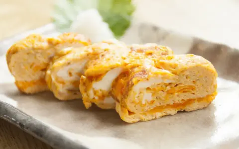 Délicieux oeuf japonais roulé, aux couches dorées et blanches, servi sur une assiette avec une feuille verte.