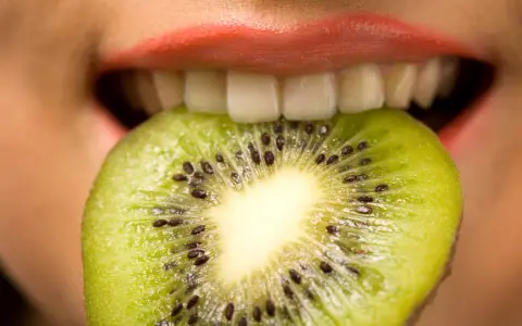 Une tranche de kiwi est mordue par des lèvres roses, ses petites graines noires contrastant avec la chair verte. Une sensation de kiwi langue qui pique.