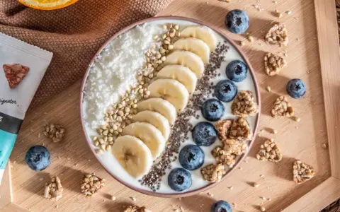 Un bol de smoothie aux bananes, myrtilles, noix de coco râpée et graines de chia, parfait pour un déjeuner au bureau sain et gourmand.