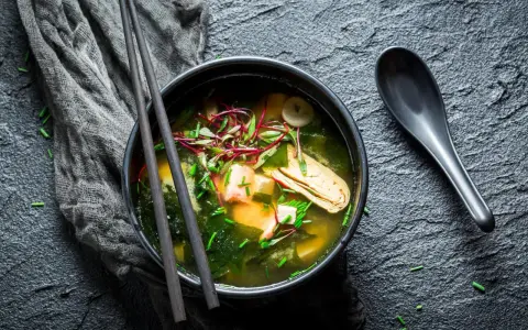 Un bol de bouillon miso fumant, garni de tofu, d'algues et de pousses rouges, prêt à être dégusté avec des baguettes.