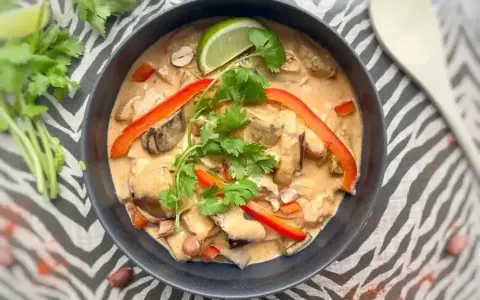 Un délicieux curry rouge, une composition appétissante avec des poivrons, de la coriandre et un quartier de citron vert.