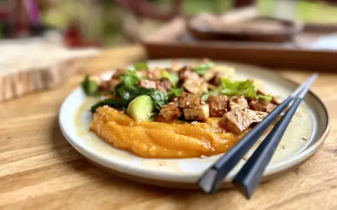 Un plat savoureux de tofu miso sur une purée de patates douces, garni de légumes verts et de graines de sésame.