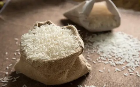 Un sac en toile de jute déborde de riz blanc, une céréale essentielle. Une autre bourse de riz est visible en arrière-plan.