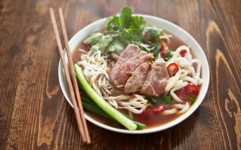 Un bol de soupe nouille de riz avec du bœuf, des germes de soja, des oignons verts et du piment rouge, prêt à être dégusté avec des baguettes.