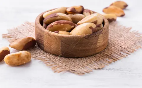 Un bol en bois rempli de noix du Brésil, mettant en avant leurs bienfaits nutritionnels. Quelques noix sont dispersées autour.