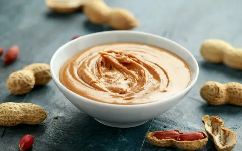 Un bol de sauce cacahuète facile, crémeuse et onctueuse, entouré de cacahuètes entières et décortiquées.
