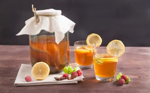Bocal de kombucha et deux verres garnis de citron, framboises et menthe. Découvrez les kombucha bienfaits pour une boisson rafraîchissante et saine.
