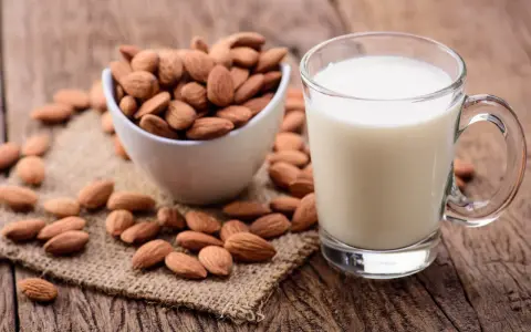 Un verre de lait d'amande frais à côté d'un bol d'amandes entières sur une surface en bois rustique.