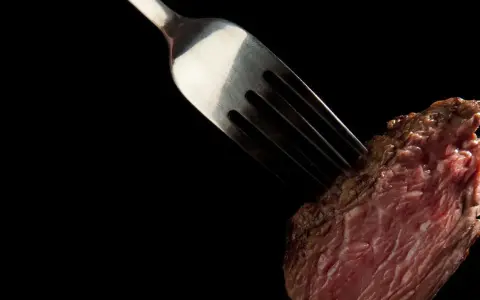 Une fourchette transperce un morceau de viande rouge, rappelant la prudence pour ceux qui ont une allergie au porc.