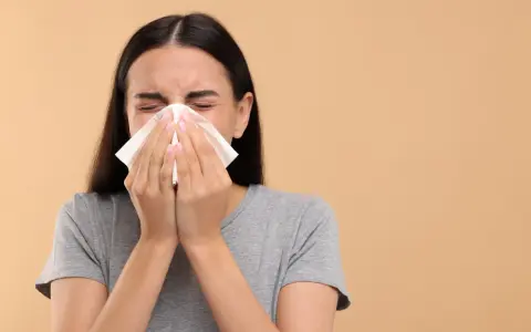 Une jeune femme se mouche dans un mouchoir en papier, le nez bouché par un rhume.