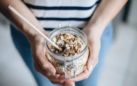 Mains de personne tenant un bocal en verre rempli de muesli maison, avec une cuillère en bois.