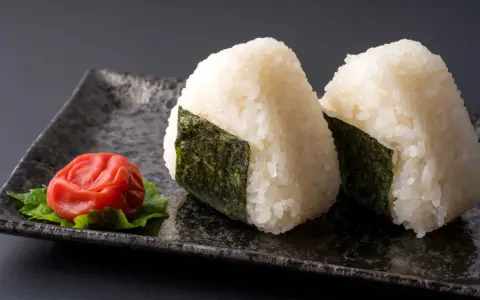 Deux onigiri algue sur une assiette avec une prune salée.
