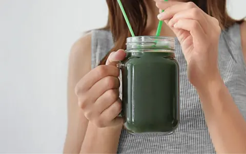 Une femme boit un smoothie vert à la spiruline, un allié pour la santé et la beauté des cheveux.