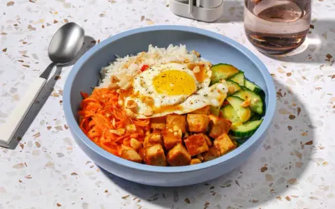 Un bol de bibimbap tofu avec riz, carottes râpées, concombre, œuf au plat et cacahuètes concassées.