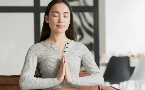 Jeune femme méditant, mains jointes, pour apprendre comment reduire le stress naturellement.