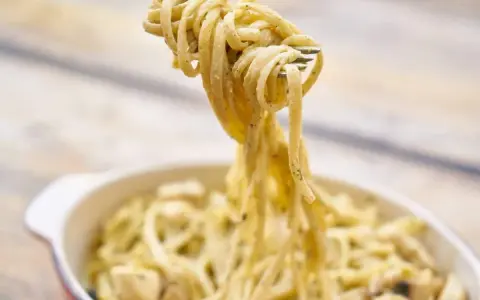 Une fourchette soulève des pâtes crémeuses, peut-être des pâtes cacahuète, d'un plat.