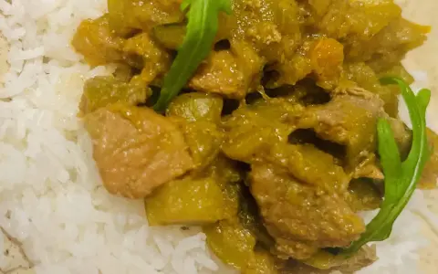 Un plat de riz blanc garni d'un curry vert aux légumes et morceaux de viande.