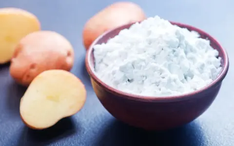 Fécule de pomme de terre dans un bol, avec des pommes de terre coupées en arrière-plan. Idéal pour savoir par quoi remplacer la fécule de pomme de terre.