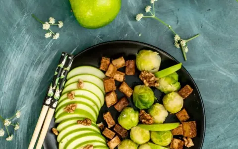 Salade colorée avec des tranches de pomme verte, des choux de Bruxelles, des dés de tofu croustillant et des noix, le tout arrosé d'une vinaigrette miso.