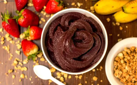 Un bol de sorbet **açaí** onctueux, entouré de fraises, bananes et granola. Une cuillère blanche est posée à côté.