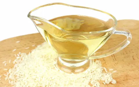 Un vinaigrier en verre rempli de liquide doré, entouré de grains de riz. Une idée pour par quoi remplacer le vinaigre de riz.