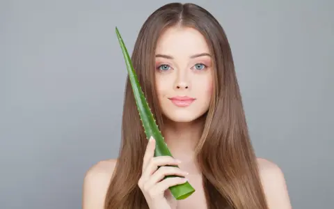 Une jeune femme aux cheveux longs tient une feuille d'aloe vera, montrant comment utiliser l'aloe vera pour une peau éclatante.