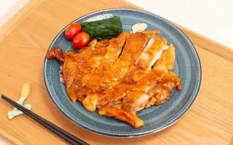 Délicieux poulet teriyaki recette, tranché et glacé, servi avec des tomates cerises et des épinards sur une assiette bleue.