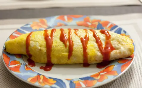 Une omelette japonaise au riz, nappée de ketchup, sur une assiette décorée de fleurs.