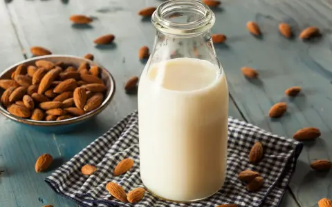Bouteille de lait végétal d'amande, avec un bol d'amandes et des amandes éparpillées sur une table en bois bleu.