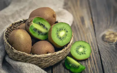 Un panier de kiwis frais, certains entiers, d'autres coupés, révélant leur chair verte et leurs pépins noirs. Attention, le kiwi peut provoquer une allergie.